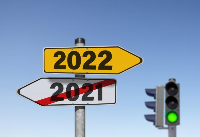 A street sign with two arrows pointing in opposite directions. The lower arrow points left and has 2021 with a red slash over it. The top arrow points right and has 2022 on it. In the background is a green traffic light, signaling that we are good to go for 2022!