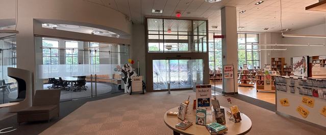 The interior of the library showing a circular meeting room to the left, displays of books and a service desk to the right, and a round table with books on display in the front center.