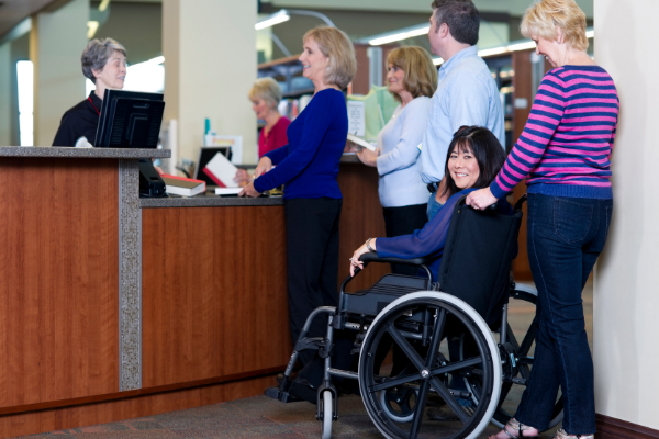 A librarian stands behind a desk, helping a group of happy patrons.