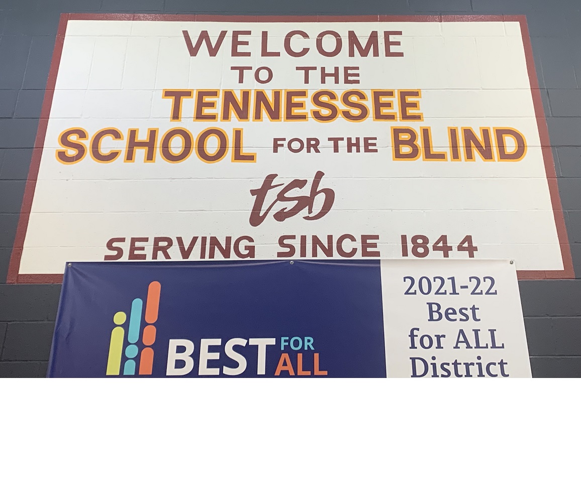A large sign painted on a wall reading Welcome to the Tennessee School for the Blind, serving since 1844, with the initials tsb in fancy script in place of a logo. Hanging beneath that is a vinyl sign reading 2021-22 Best for All District.
