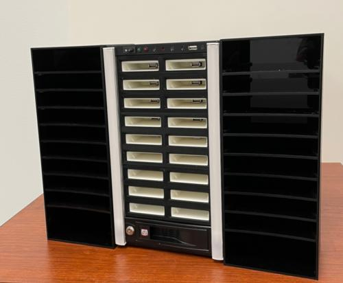The scribe 2.0 has a grid of 18 cartridge slots in two columns down the middle of the unit. On either side of the slots is a narrow white strip containing LEDs, and then a plastic shelving unit just big enough to put a mail case on each shelf, with the shorter side facing out.