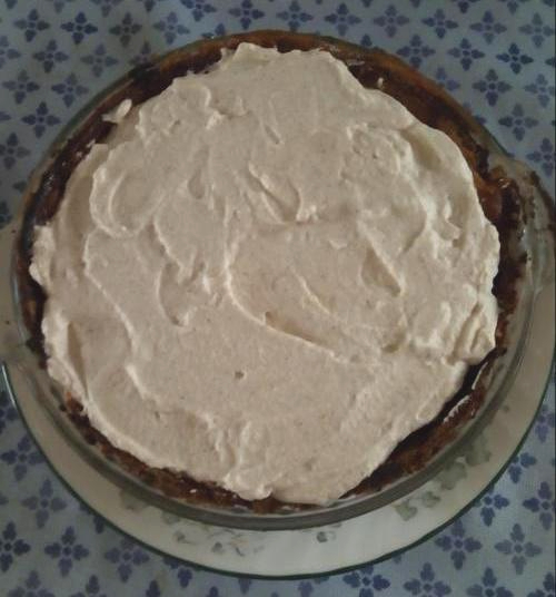 The pie is now covered in whipped cream, and is on a metal charger with a blue diamond-patterned tablecloth behind it.