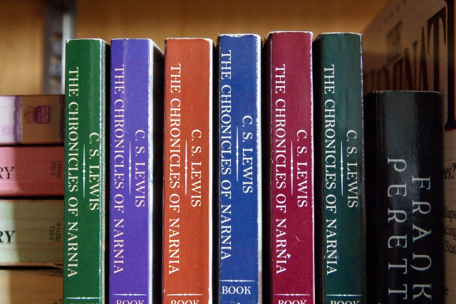 A bookshelf containing the Chronicles of Narnia series, surrounded by other books.