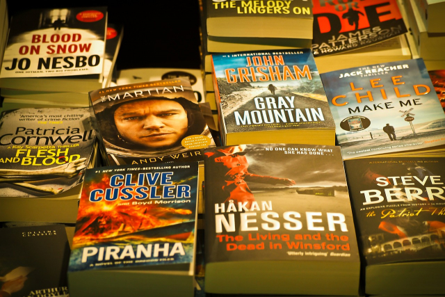A bookstore-style display of bestsellers. Visible covers include The Martian by Any Weir, Gray Mountain by John Grisham, Piranha by Clive Cussler, and the Living and the Dead in Winsford by Hakan Nesser.