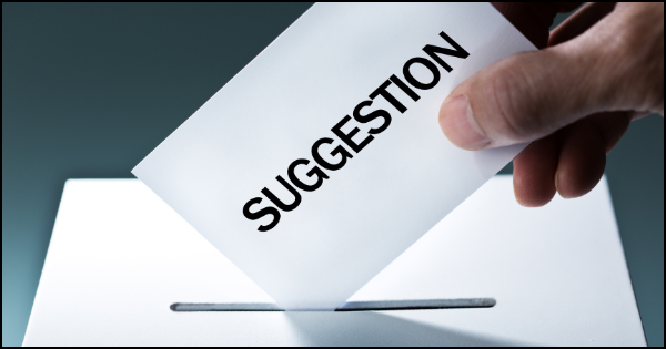 Image of someone dropping a slip of paper labeled "suggestion" into a dropbox.